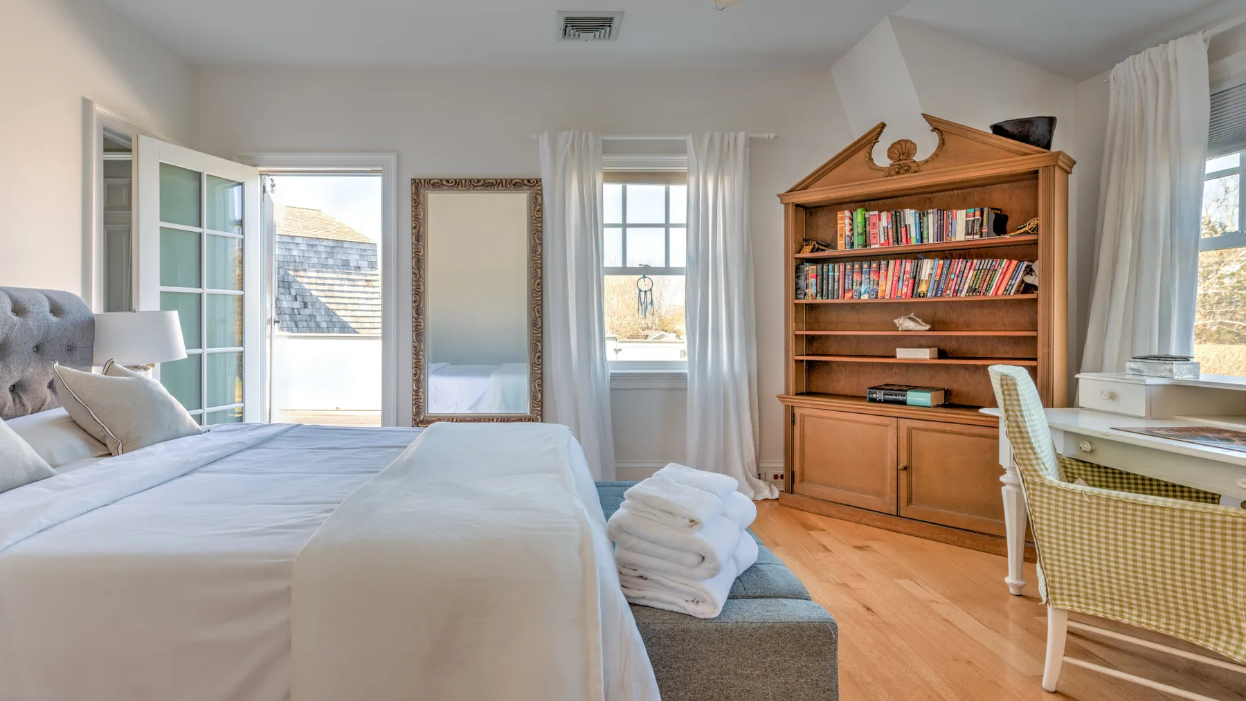 A bright bedroom with a neatly made bed and a wooden bookcase.