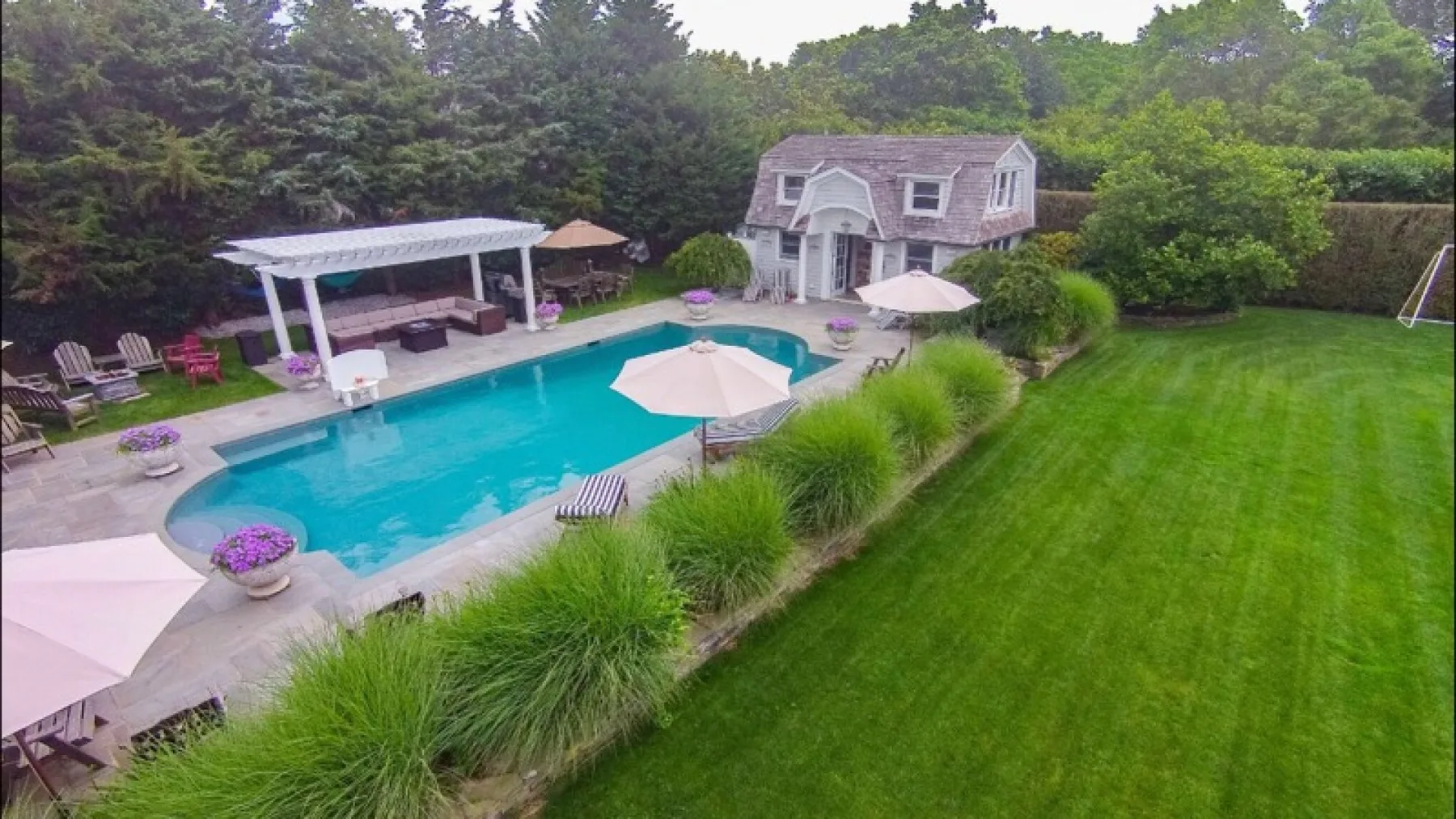 A backyard pool and lawn are bordered by patio seating and a covered pavilion.