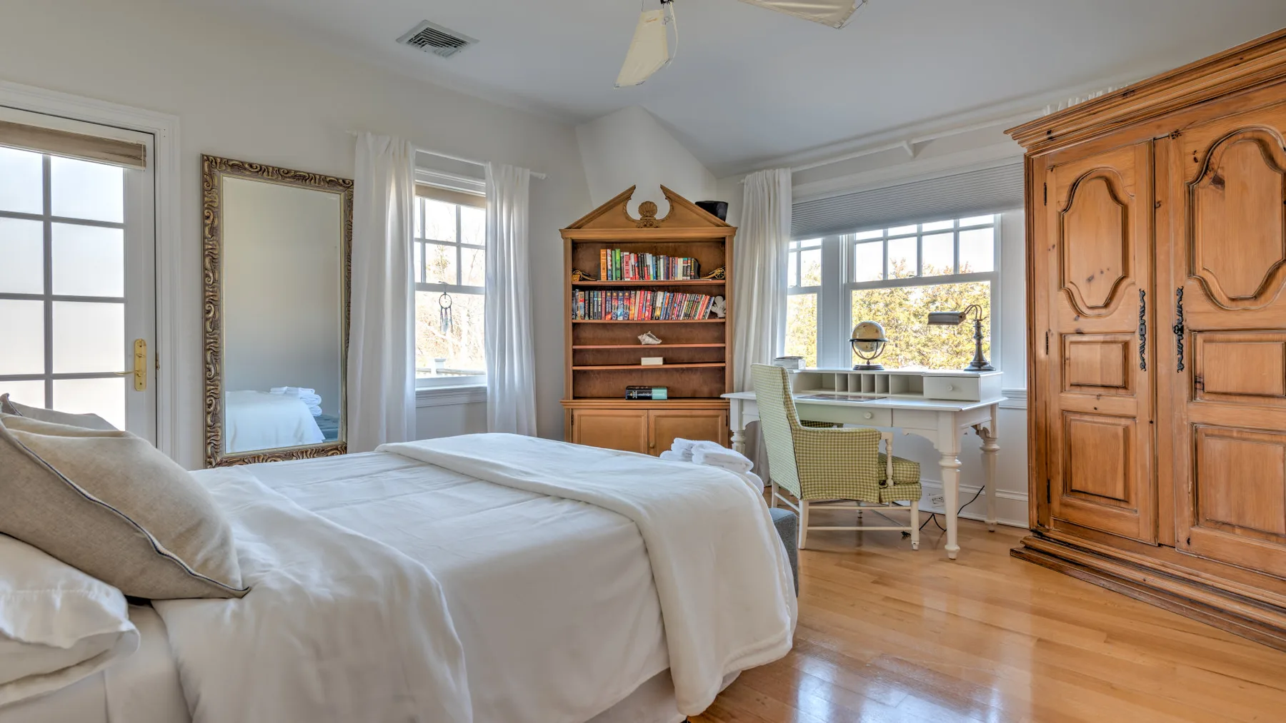 A bedroom with a bed, wooden wardrobe, and desk beside a window.