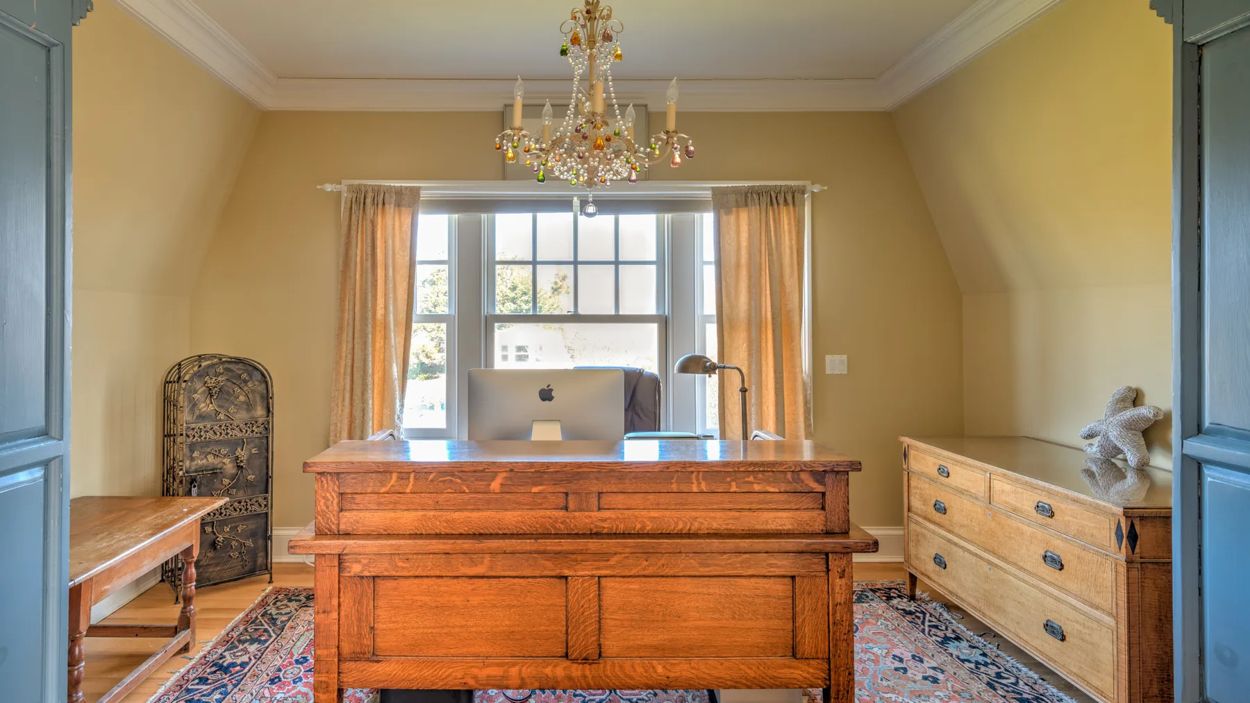 A warm-toned room with a large wooden desk beneath a chandelier.