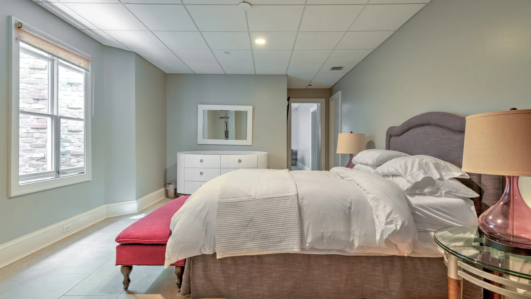 A bedroom with a bed, a window, and a red upholstered bench.