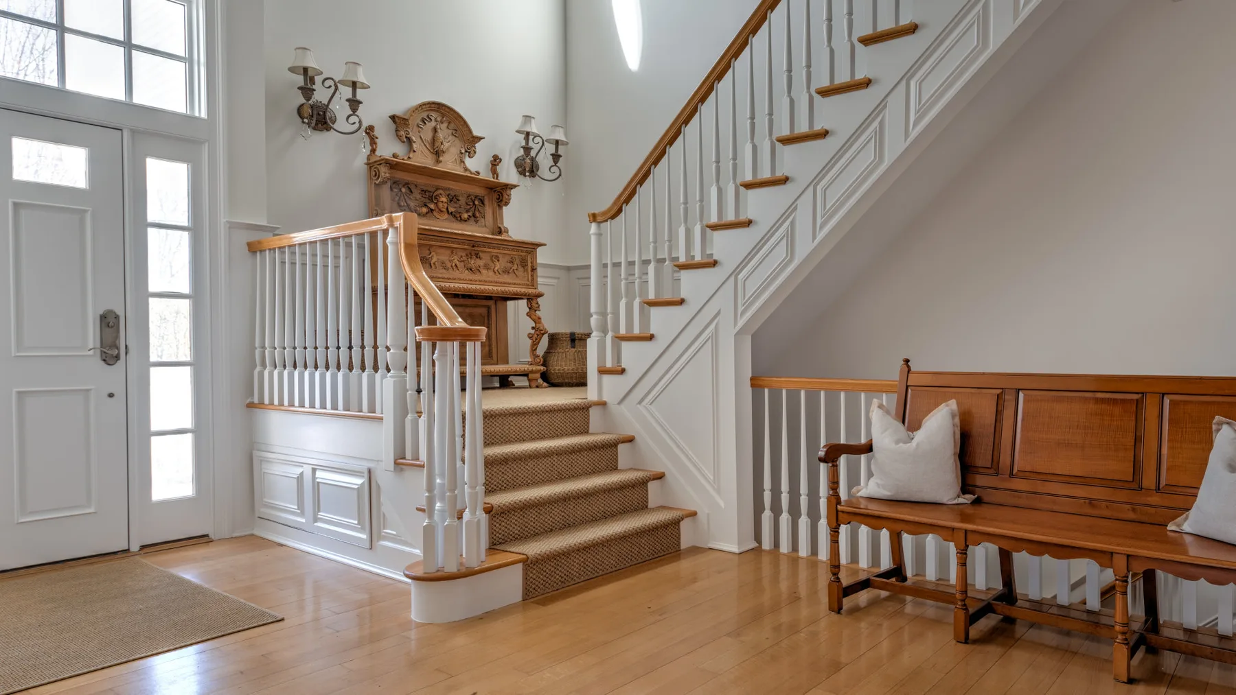 A bright entry hall with a wooden staircase and a long bench along the wall.