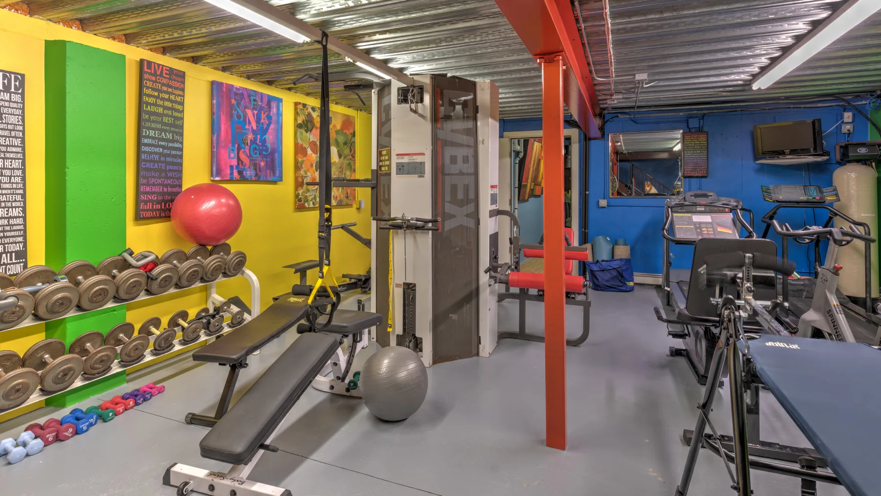 A gym with weight racks, exercise equipment, and colorful wall art.