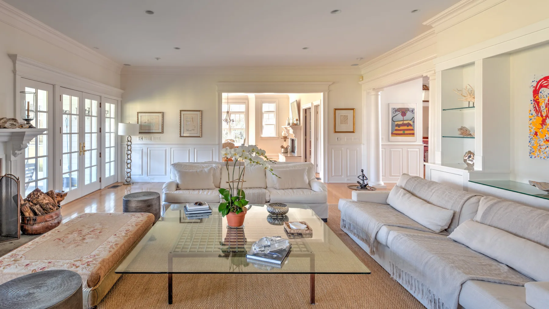 A bright living room with pale seating arranged around a glass coffee table.