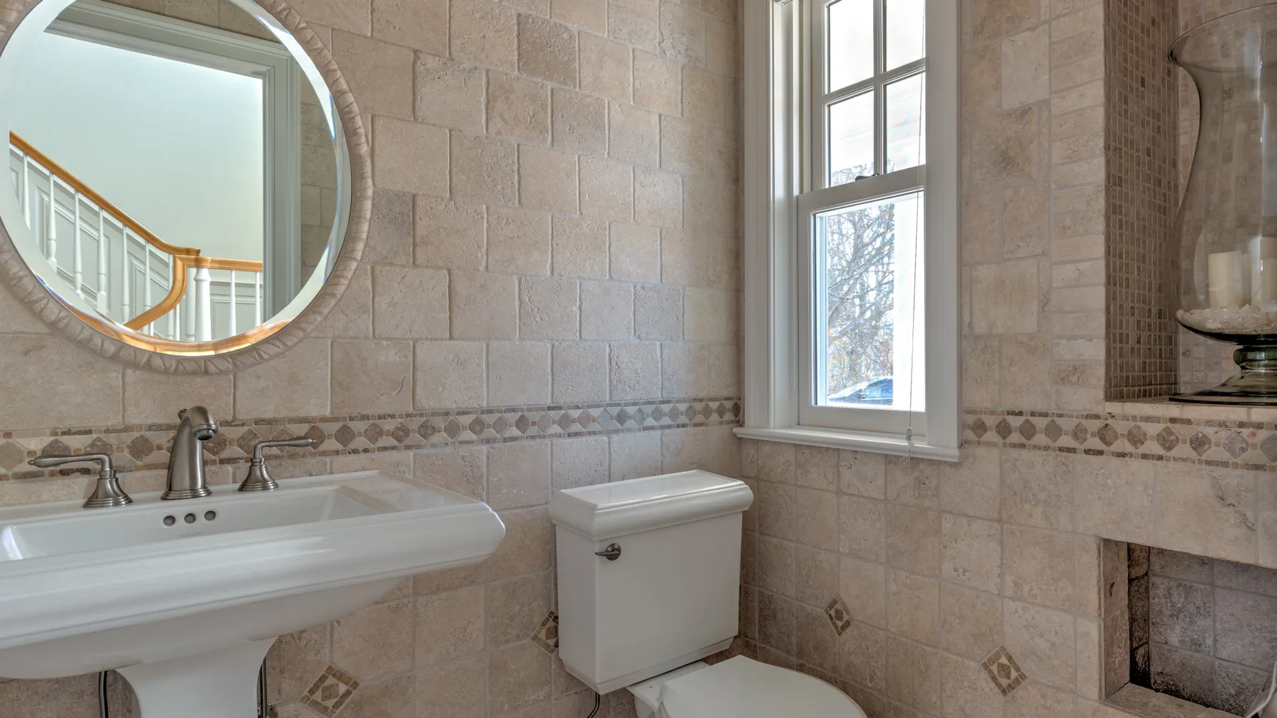 A tiled bathroom with a sink, toilet, and window.