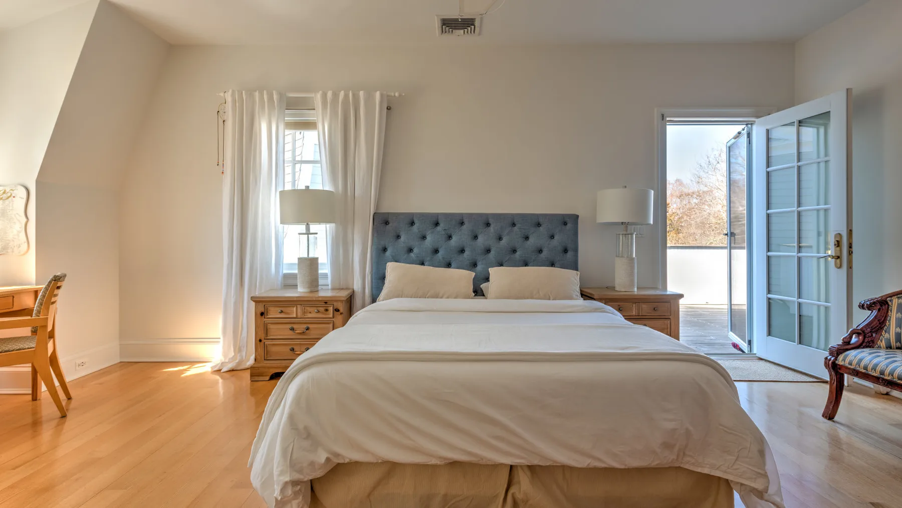 A bedroom with a neatly made bed and an open door to the outside.