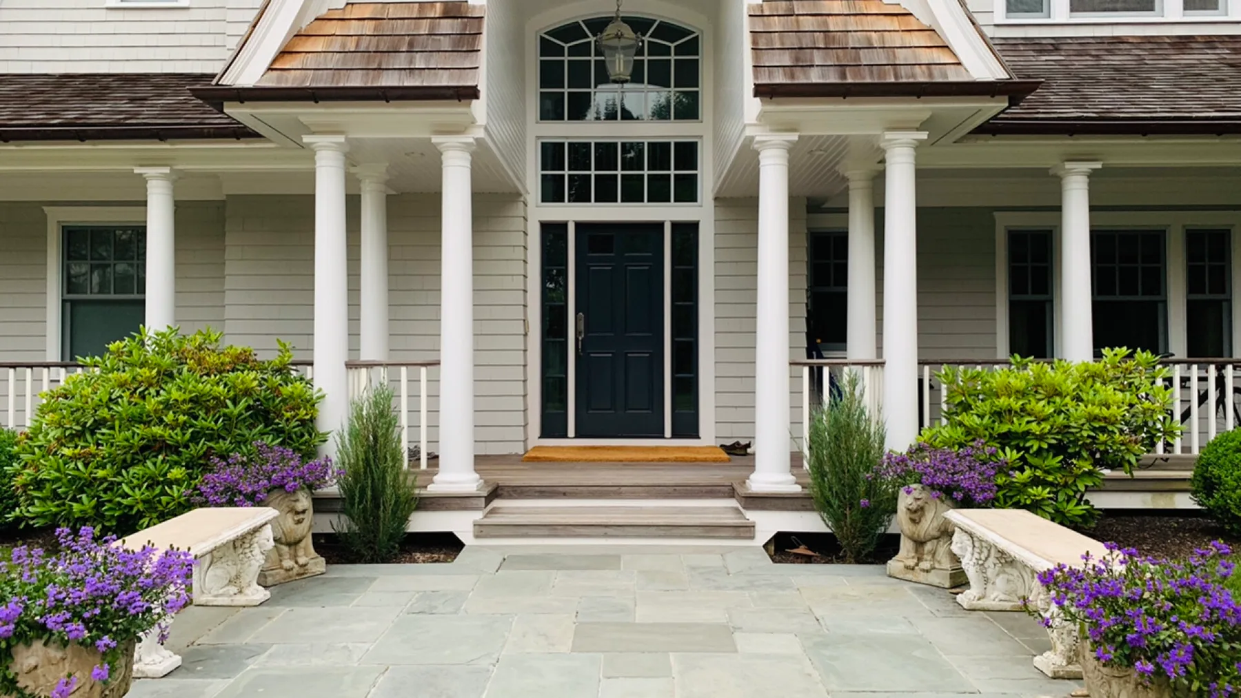 A house entrance with a dark front door, white columns, and flowering shrubs.
