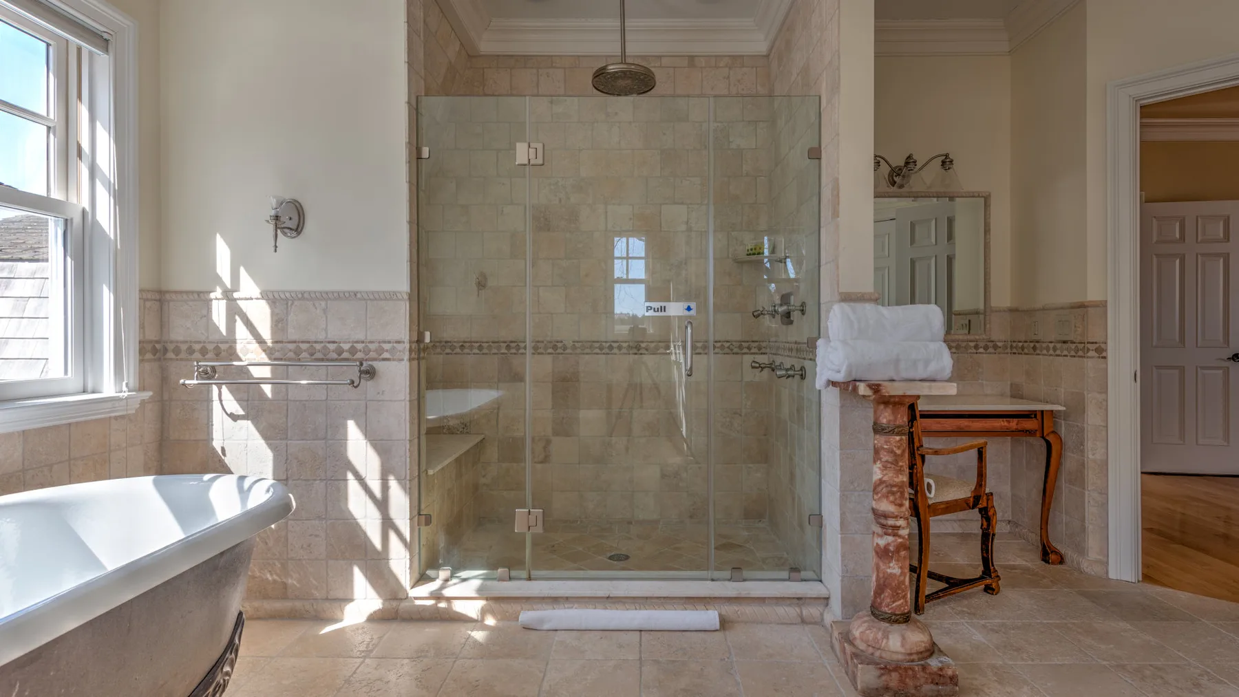 A bright bathroom with a glass shower, a bathtub, and a small vanity.