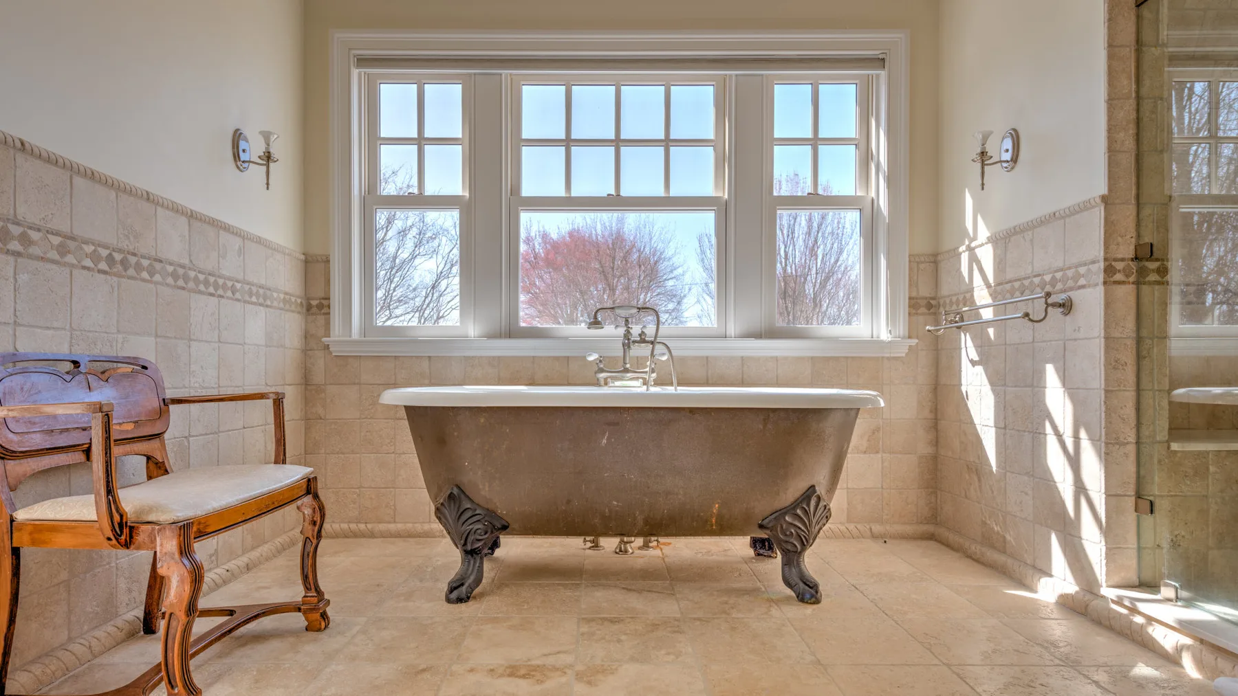 A bright bathroom features a freestanding bathtub beneath a large window.