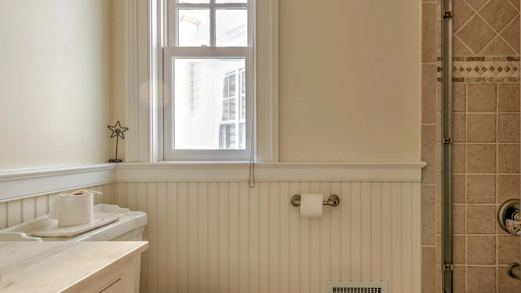 A bathroom with a window, sink, and tiled shower.