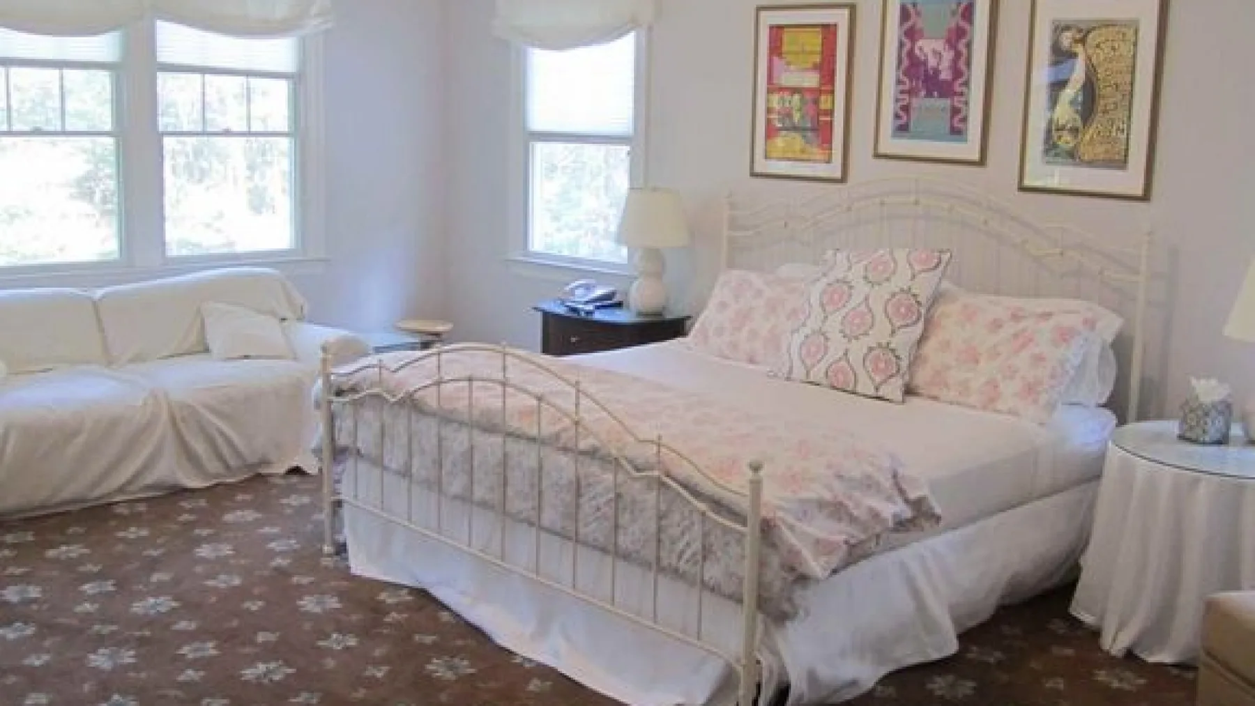 A bright bedroom with a large bed, floral bedding, and a window-side seating area.