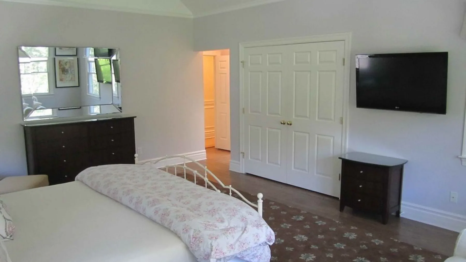 A bedroom with a bed, a wall-mounted television, and a dark dresser.