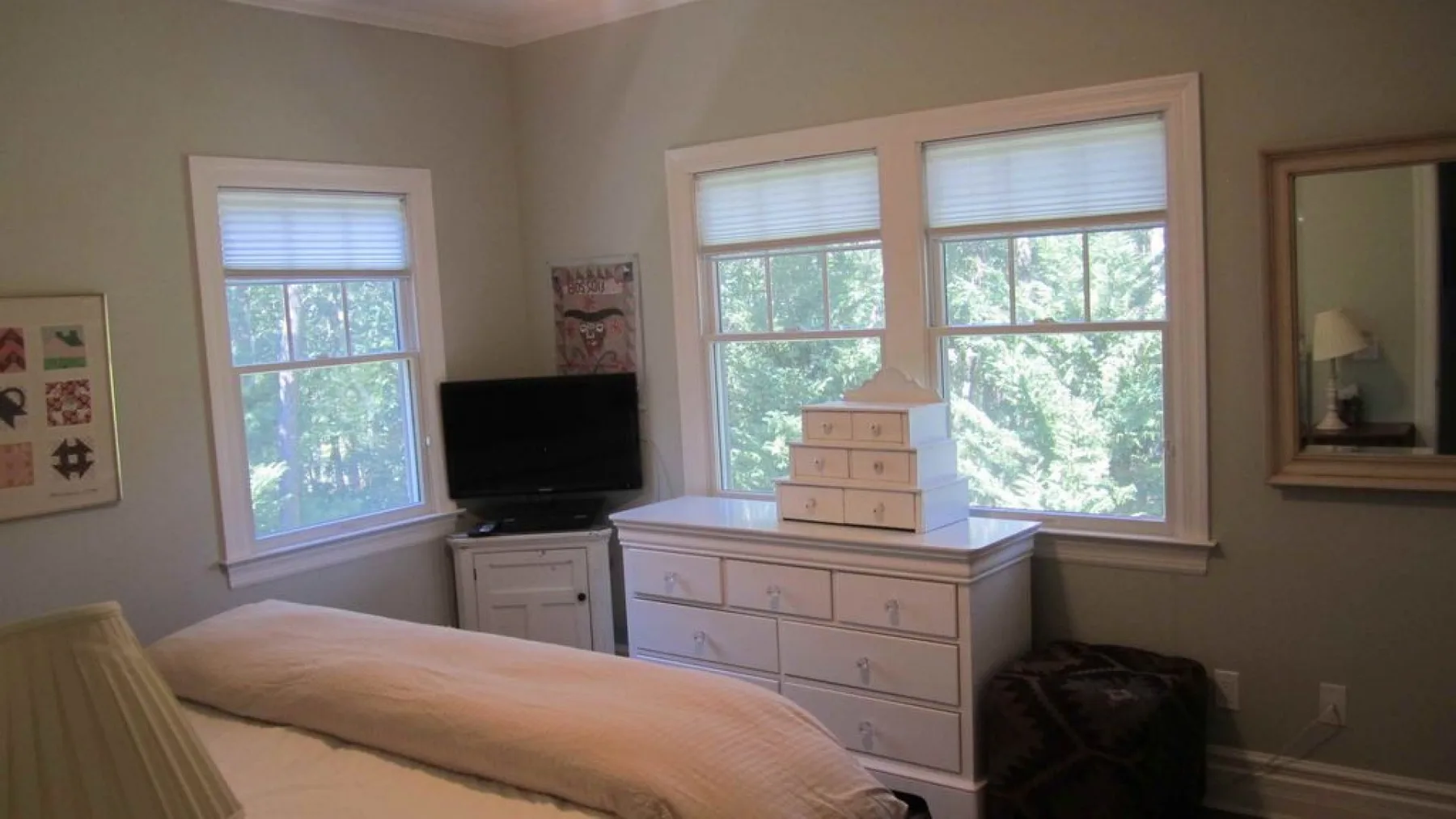 A bedroom with a bed, dresser, television, and several windows.