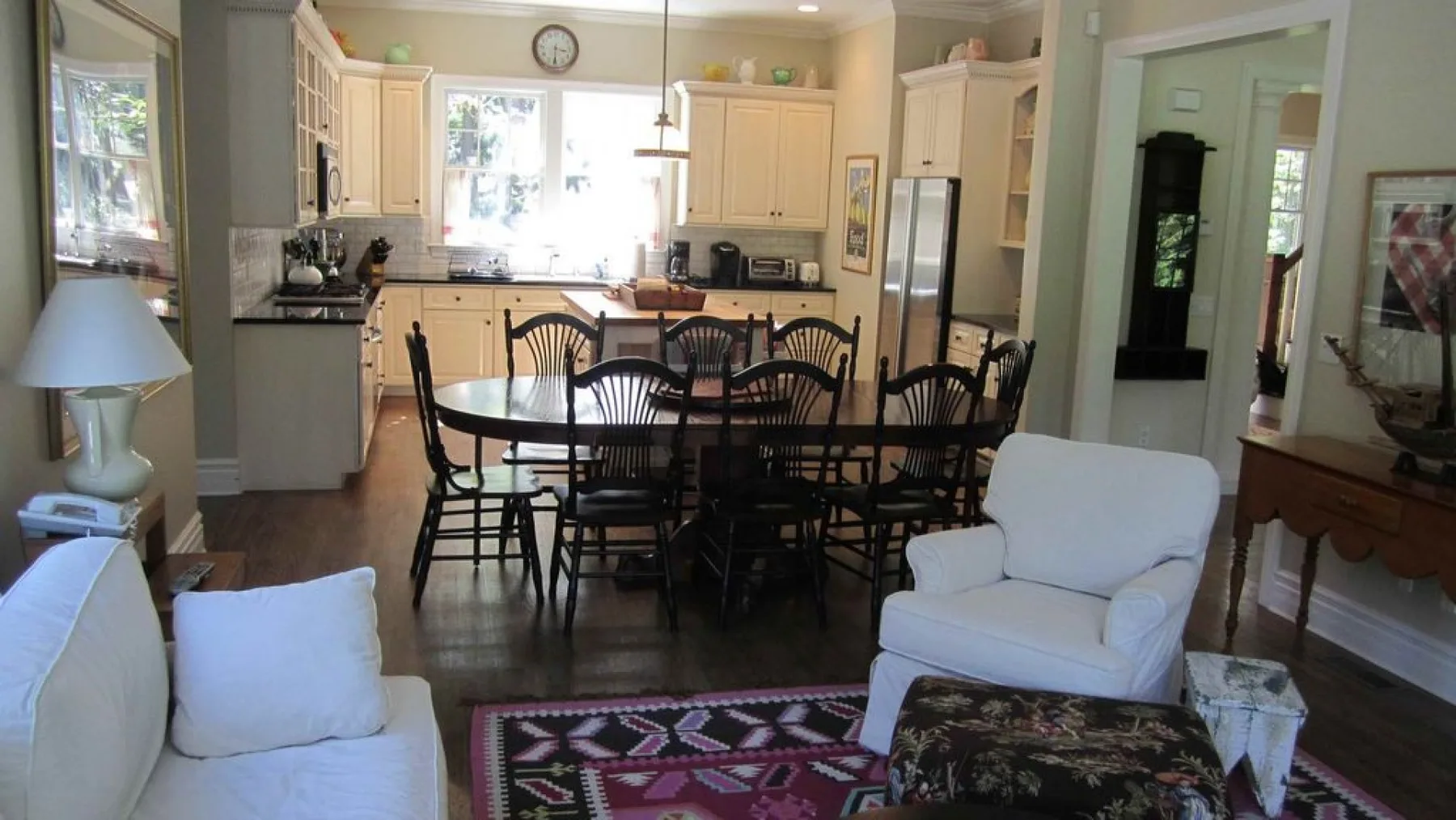 A dining area with a wooden table and chairs sits beside a living area with white seating.