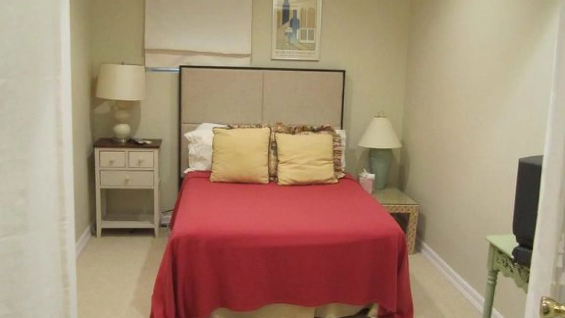 A bedroom with a bed covered in red bedding and bedside tables.