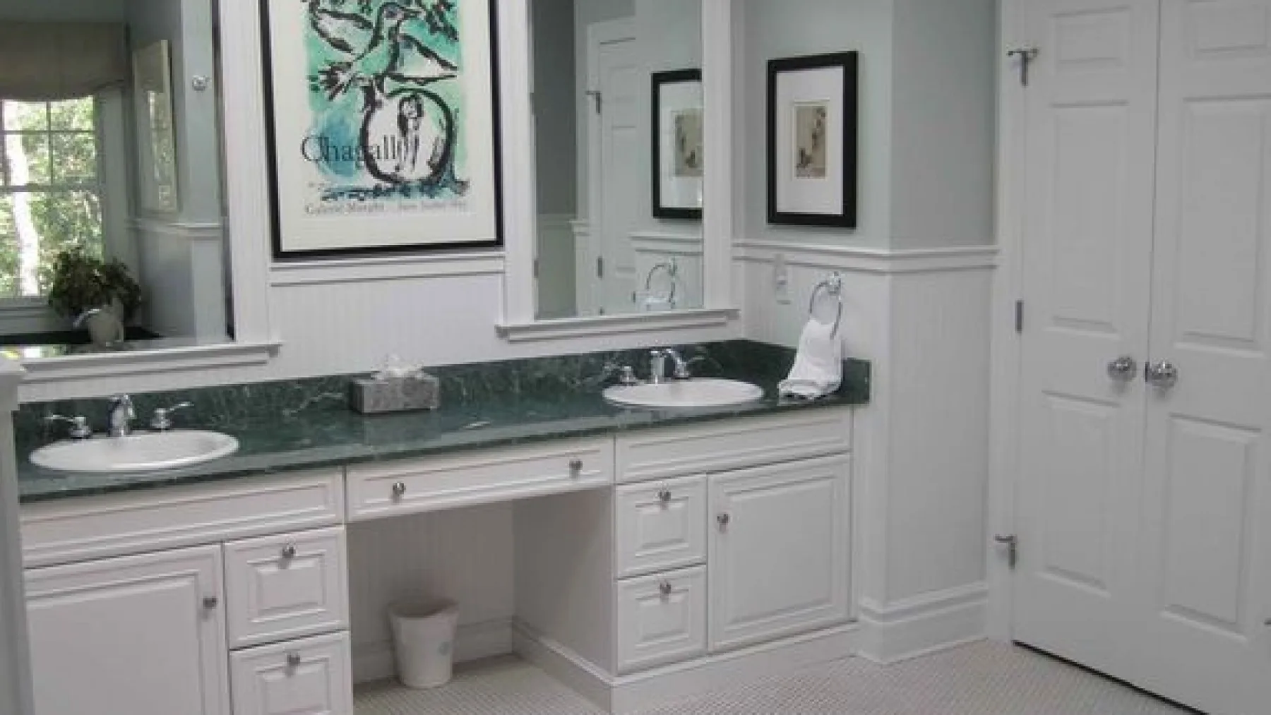 A bathroom vanity with a green countertop sits beneath a large wall mirror.