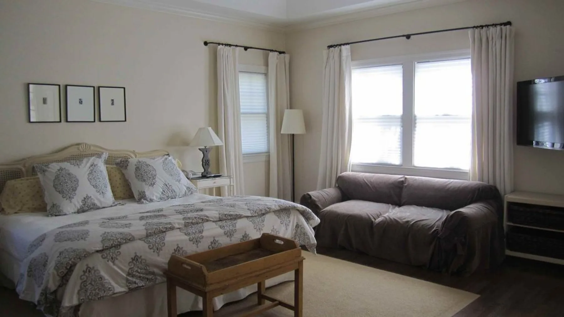 A bedroom with a patterned bed and a sofa beside the windows.