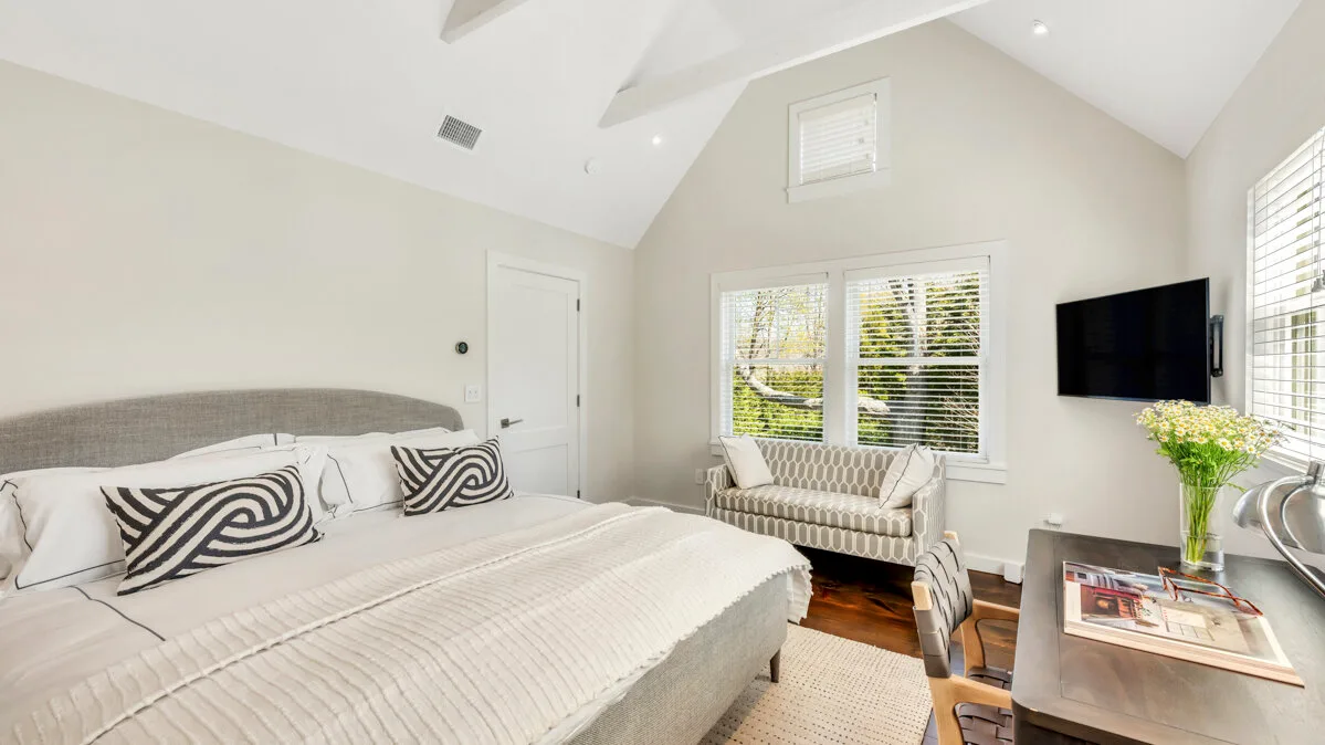Un dormitorio luminoso con una cama, asientos y ventanas grandes.