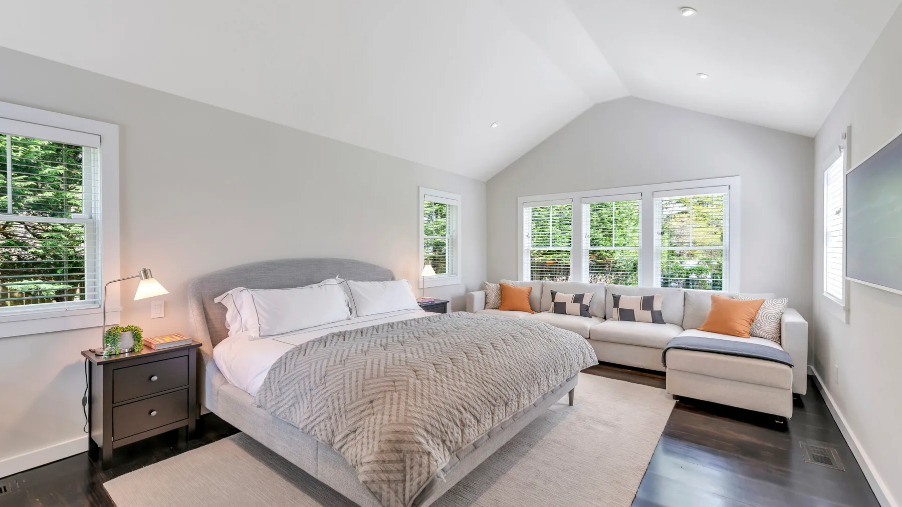 Un dormitorio luminoso cuenta con una cama grande y una zona de estar junto a amplias ventanas.