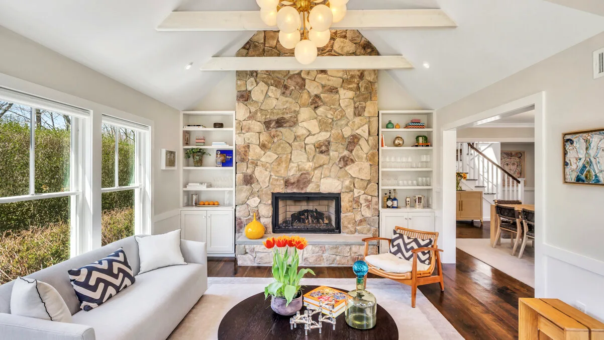 Una sala luminosa con chimenea de piedra, asientos y ventanas grandes.