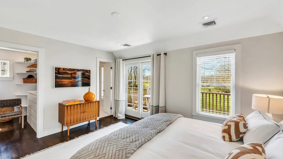 Un dormitorio con una cama, una cómoda de madera y ventanas con vista a un césped verde.
