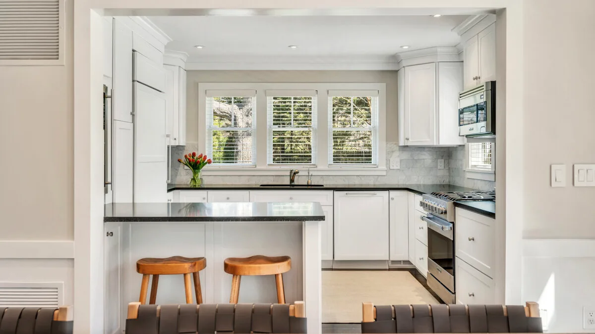 Una cocina luminosa con gabinetes blancos, una isla central y ventanas sobre el fregadero.