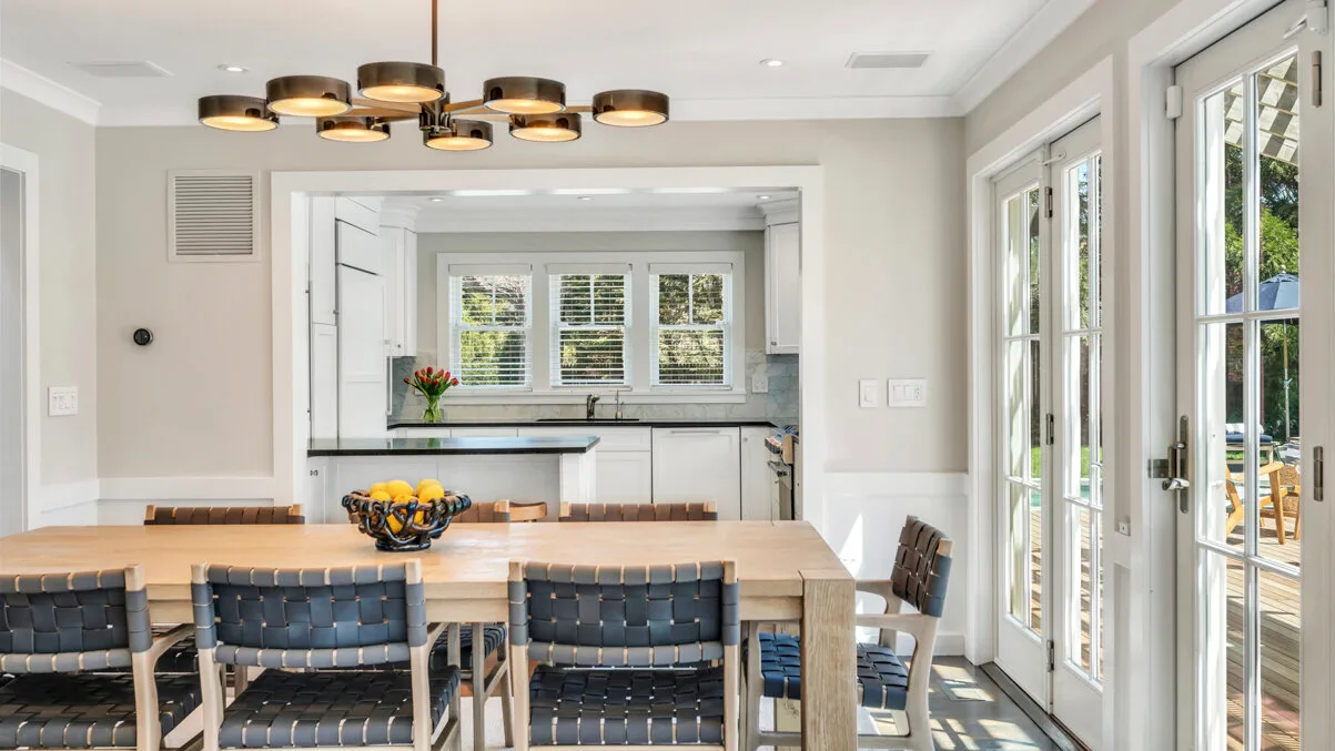 Un comedor luminoso se abre a una cocina, con grandes ventanas a un lado.