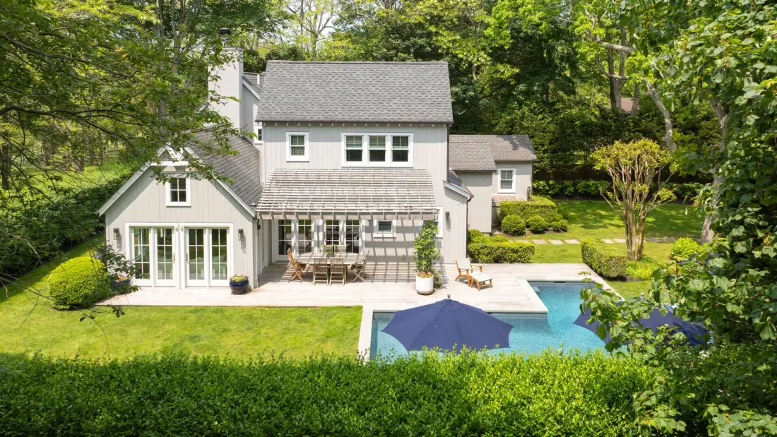 Una casa grande y una piscina están rodeadas de césped y árboles.