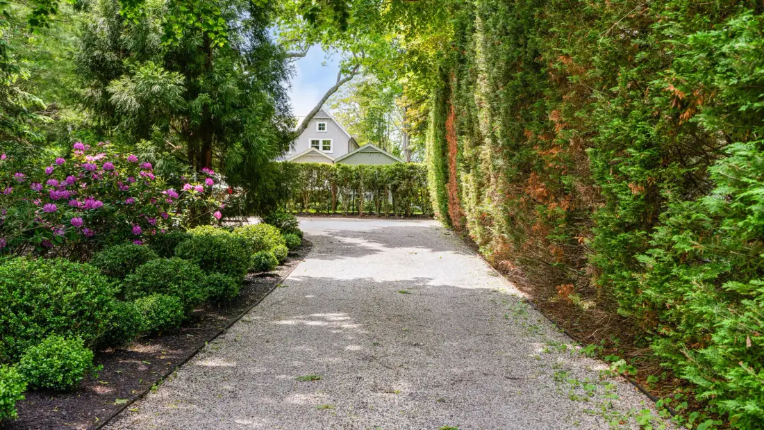 Un camino de entrada ajardinado pasa entre setos frondosos hacia una casa.