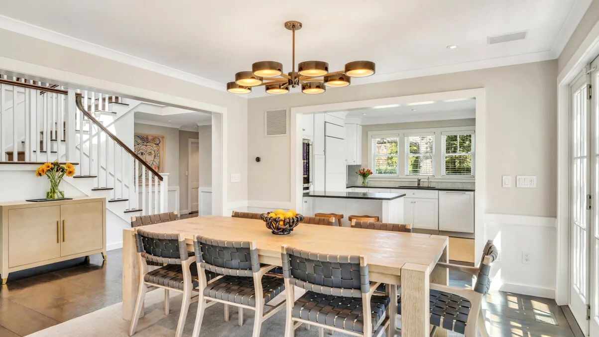Un comedor luminoso con una mesa larga junto a una escalera y la cocina.