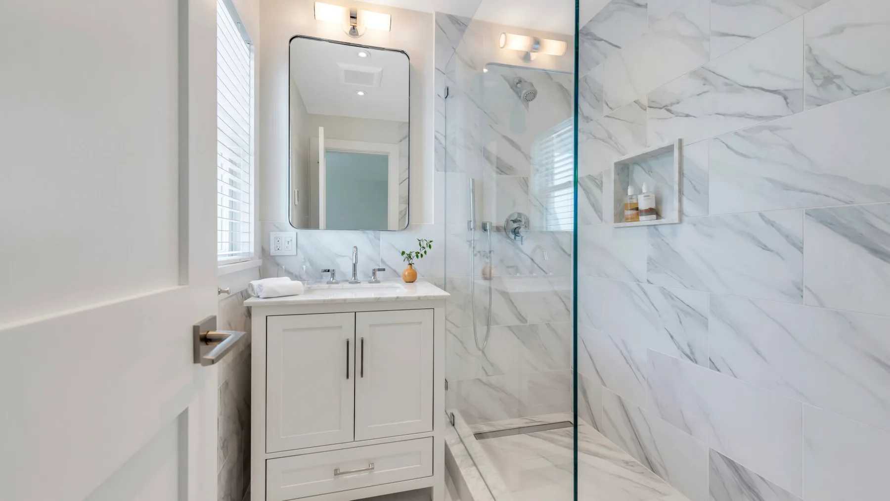 Un baño luminoso con lavabo, espejo y ducha de vidrio.