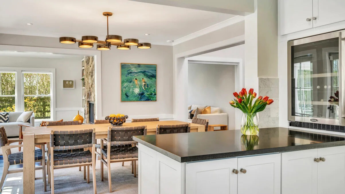 Un comedor luminoso integrado con la cocina, con una mesa, una isla y una obra de arte colorida.