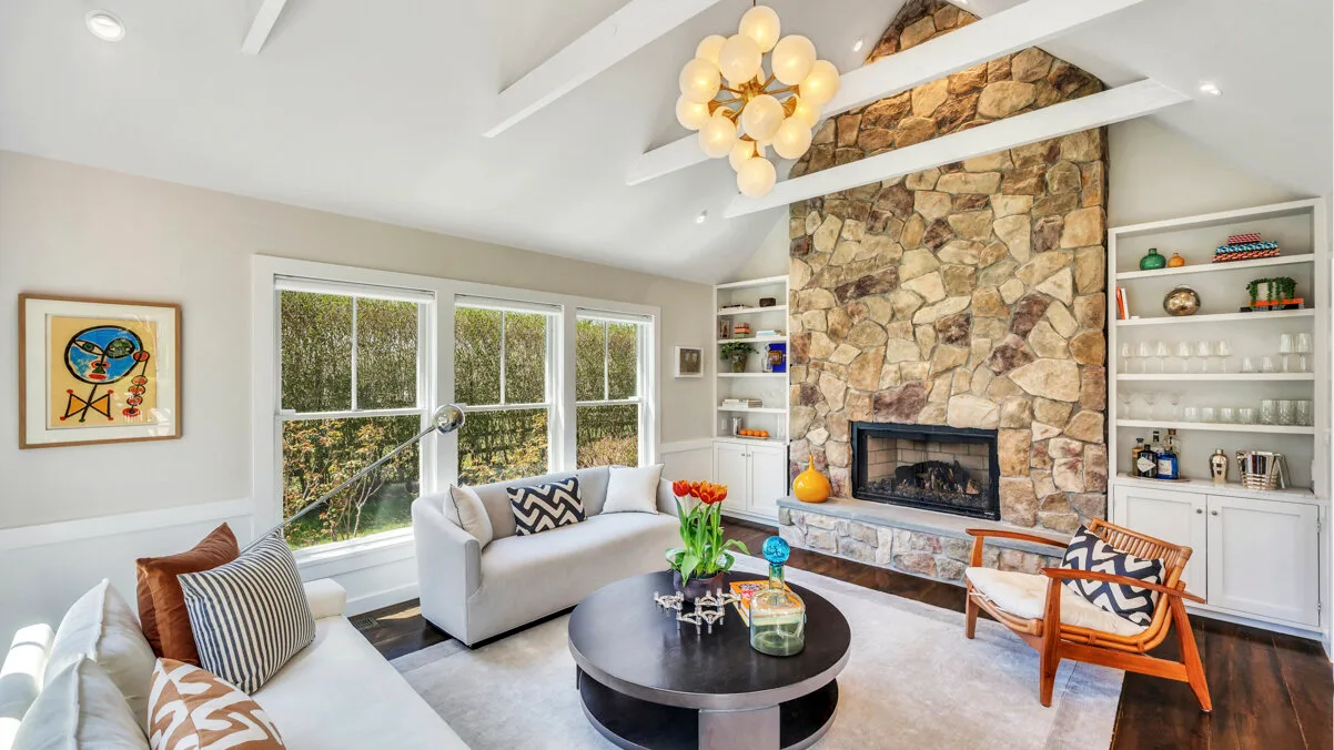 Una sala luminosa con asientos, grandes ventanas y una chimenea de piedra.