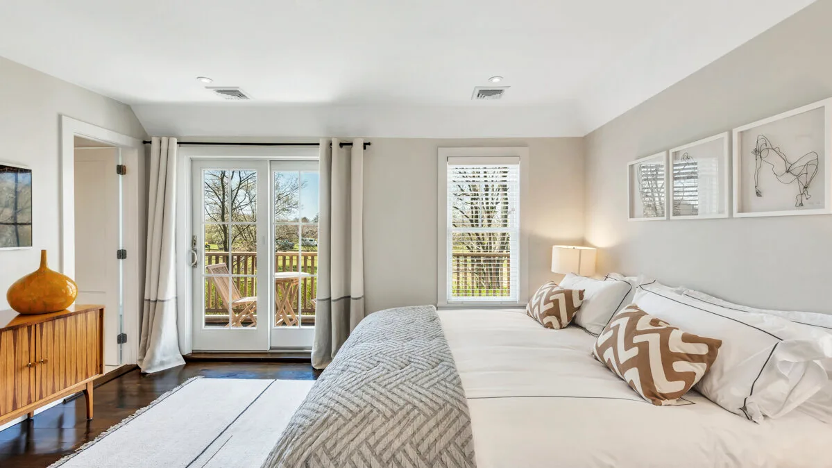 Un dormitorio luminoso con una cama junto a ventanas altas y un balcón.
