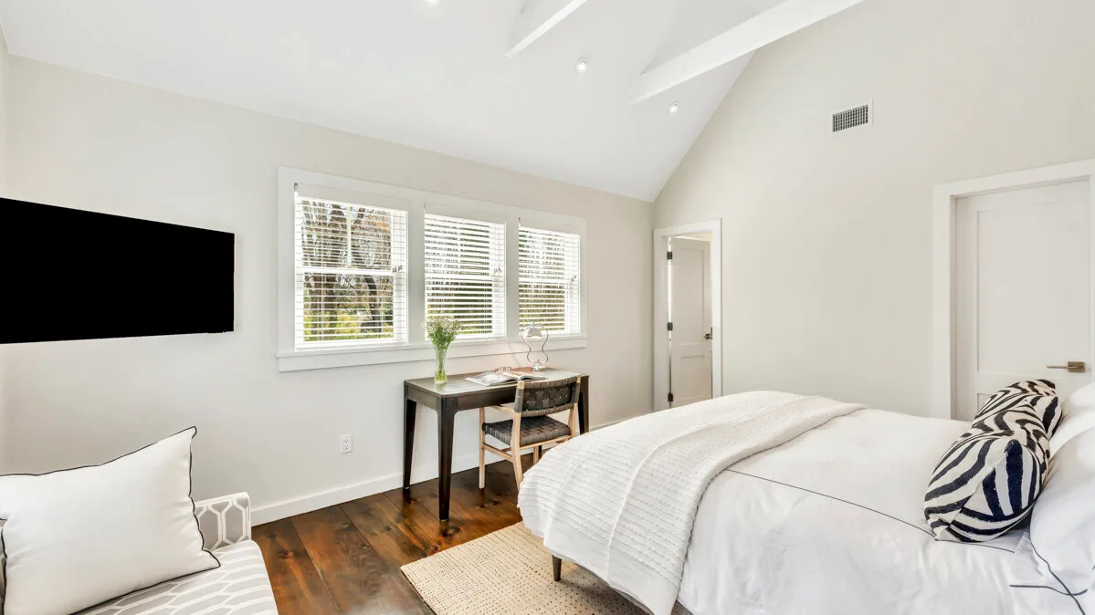 Un dormitorio luminoso con una cama, un escritorio y ventanas con persianas.