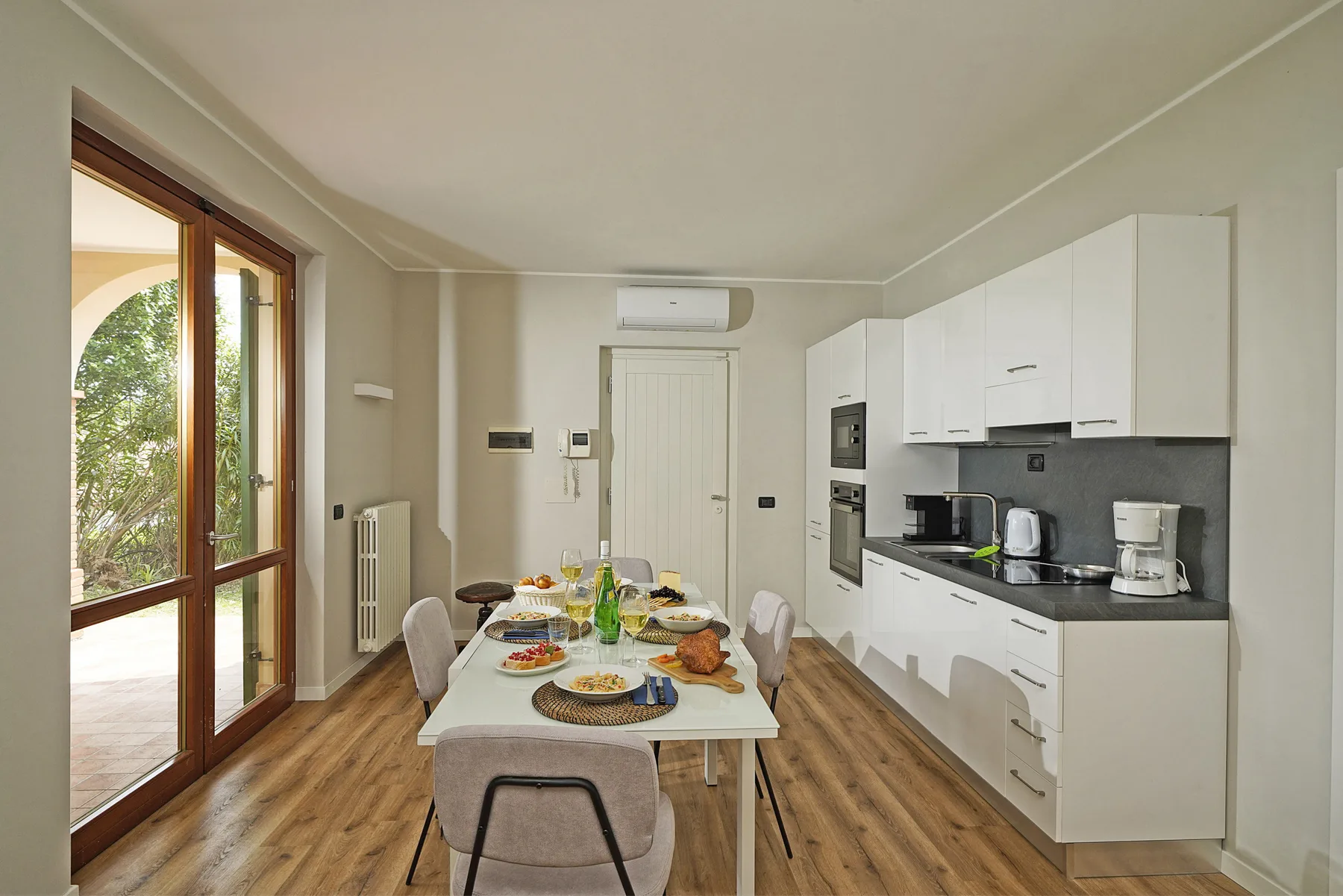 Una mesa de comedor y una cocina ocupan una habitación luminosa con grandes ventanas.