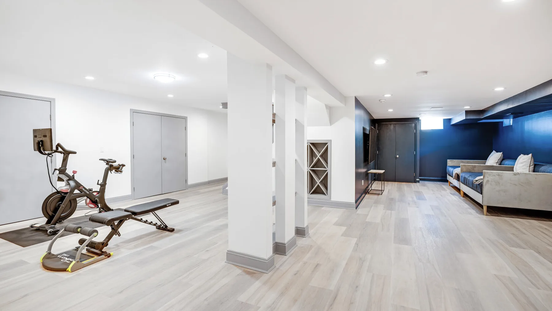 A basement recreation room with exercise equipment, seating, and a television.