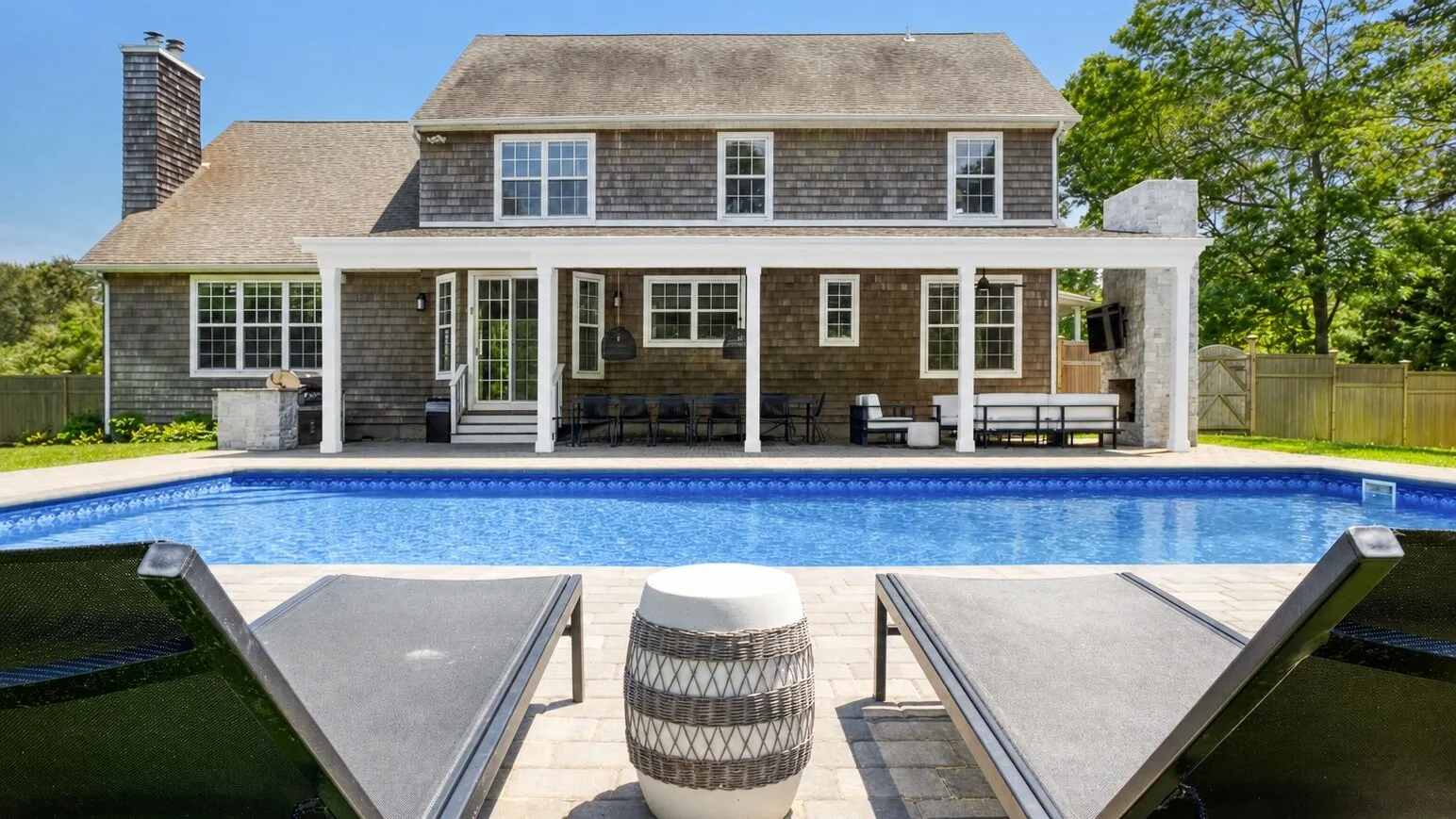 A house with a covered patio overlooks a swimming pool.