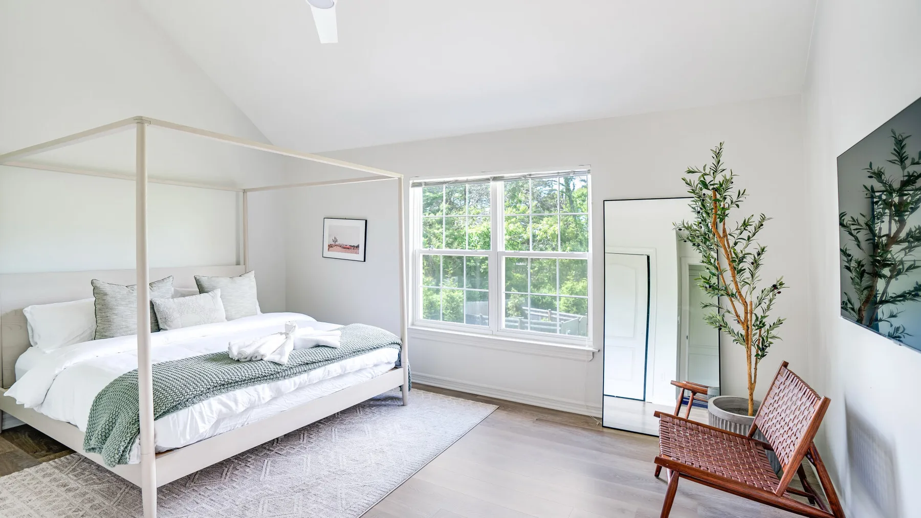 A bright bedroom with a canopy bed, large window, and a wooden chair.
