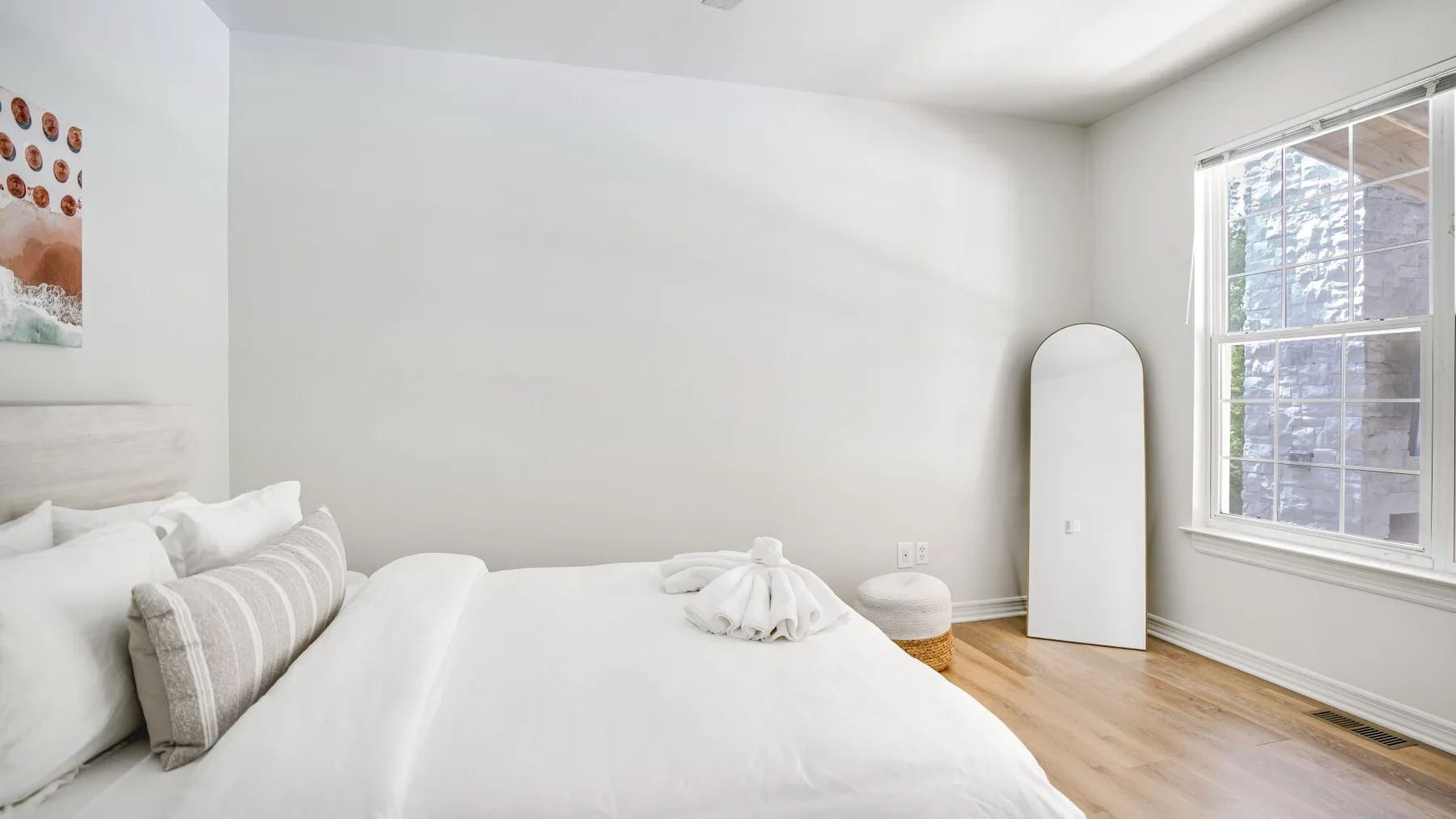 A bright bedroom with white bedding, a window, and light wood flooring.