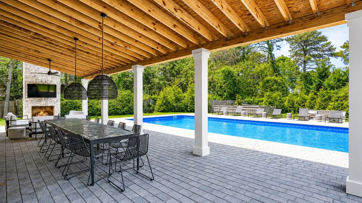A covered outdoor dining area overlooks a swimming pool and surrounding greenery.