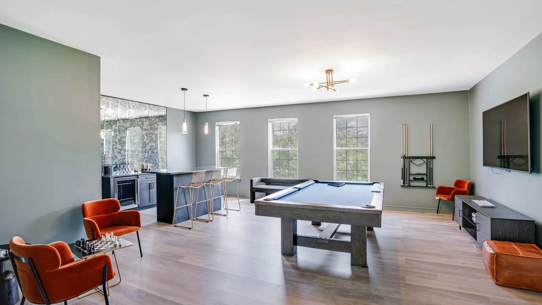 A recreation room with a pool table, seating, and a small bar area.