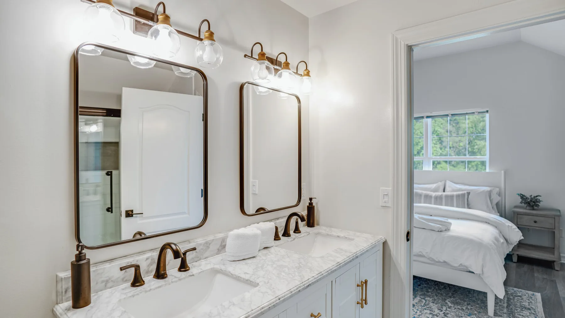 A bathroom vanity with two sinks and mirrors opens onto a bedroom.