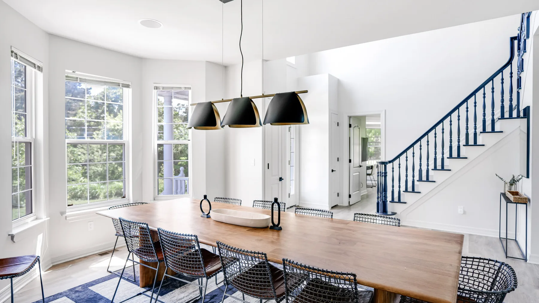 A bright dining area with a long wooden table beneath pendant lights.