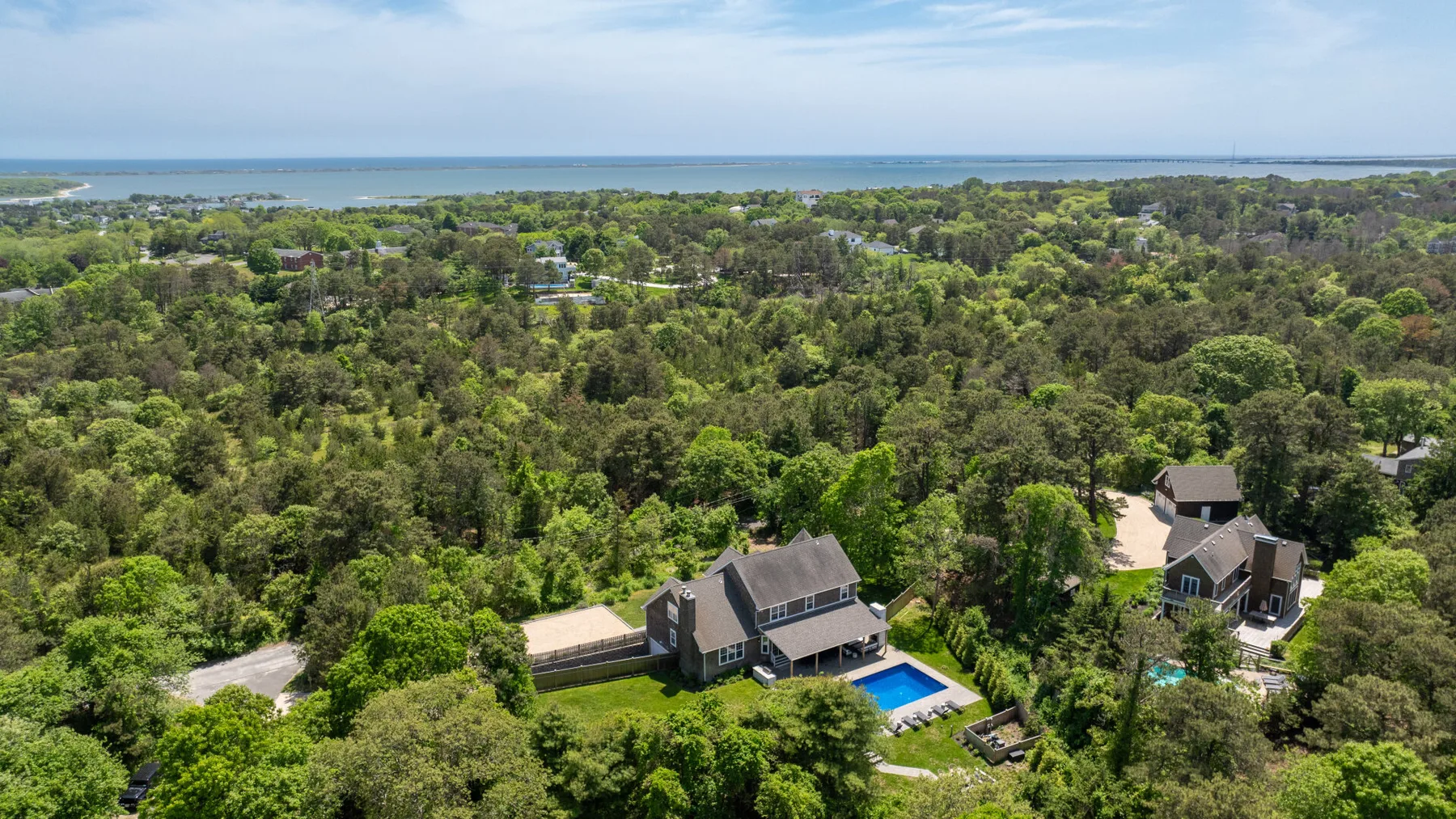 Aerial view of homes surrounded by trees, with the coastline in the distance.