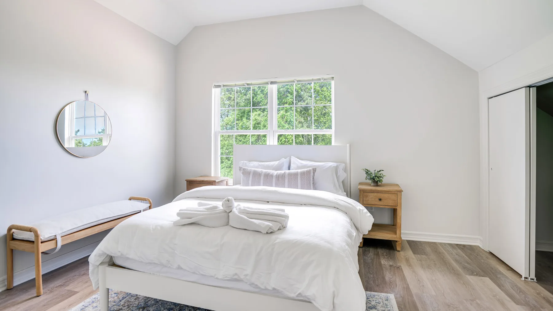 A bright bedroom with a neatly made bed beneath a large window.