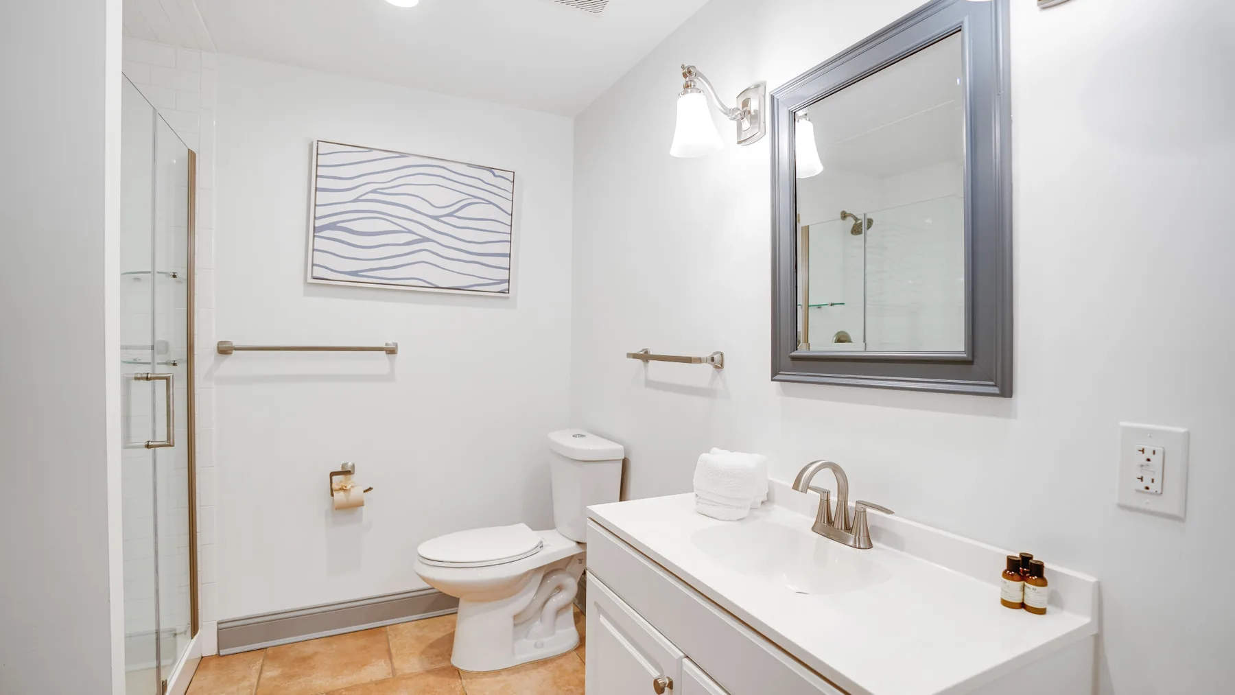 A bright bathroom with a vanity, toilet, and glass shower.
