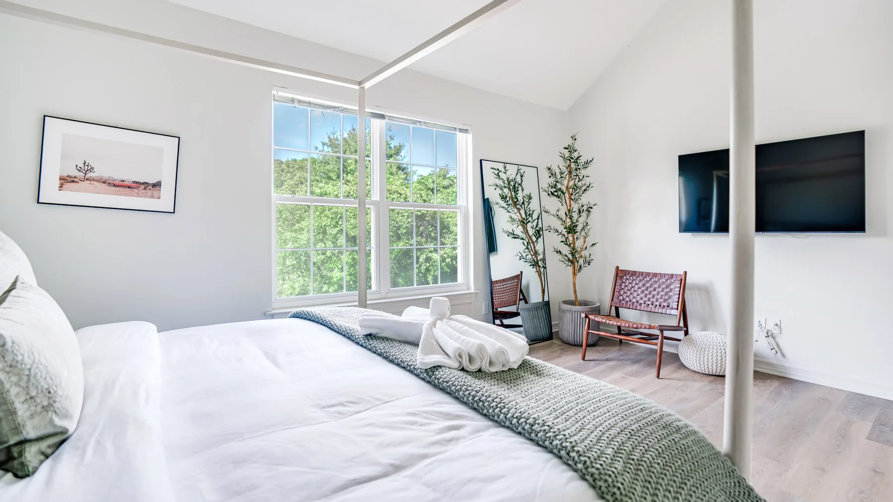 A bright bedroom with a large bed, tall windows, and two chairs.