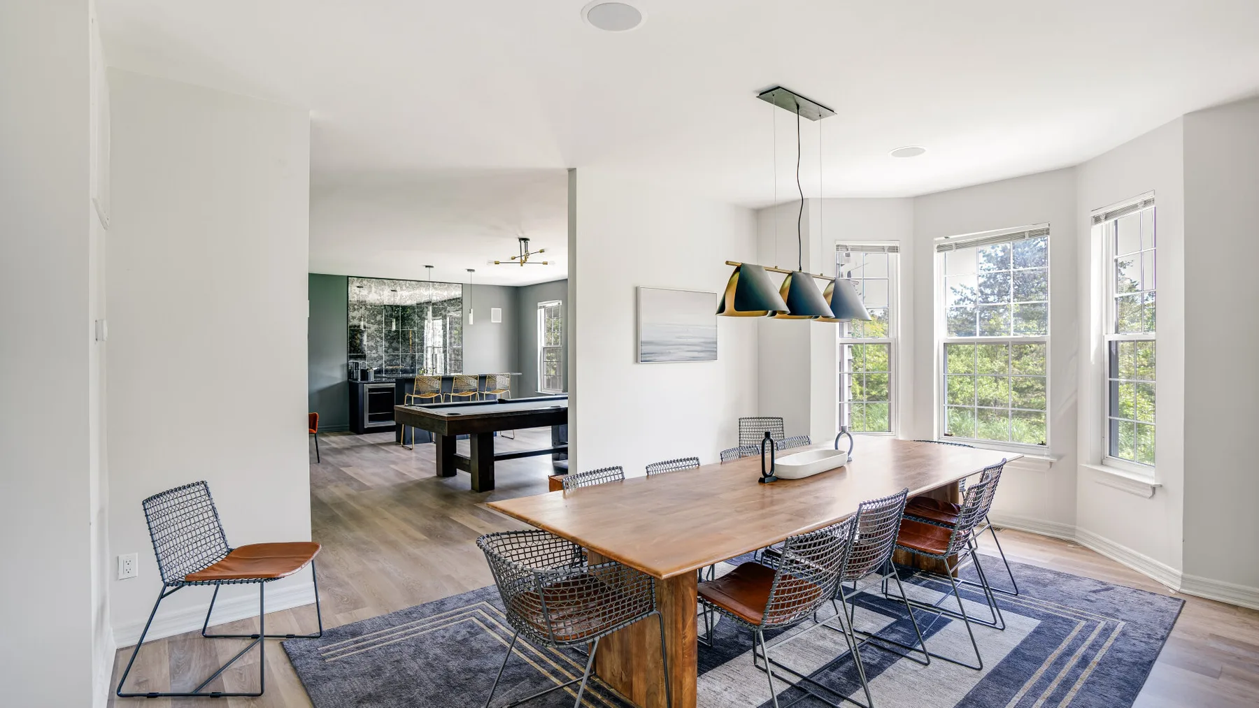 A bright dining area has a wooden table, metal seating, and large windows.