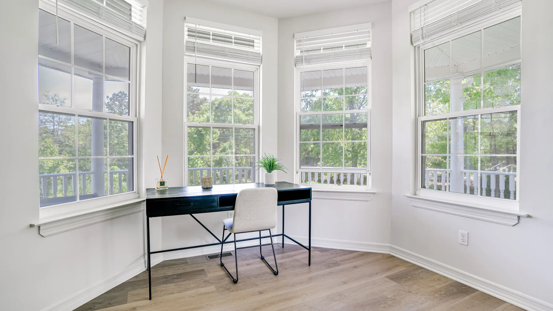 A bright room with a desk and chair positioned between large windows.